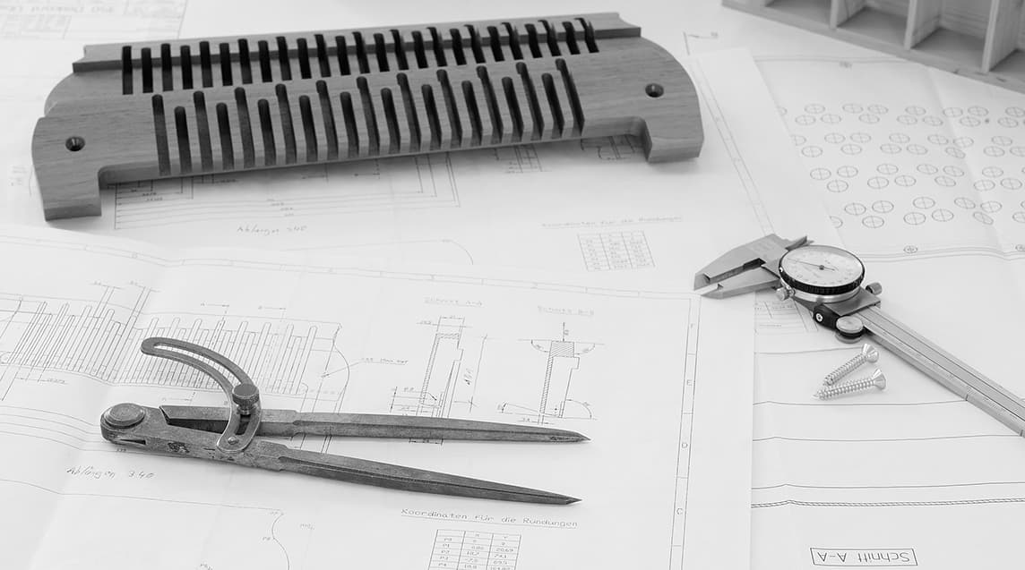 Stimmstock aus dem Tonkammer-Bau auf Werkstatt-Tisch, daneben Konstruktionspläne, Zirkel und Messschieber